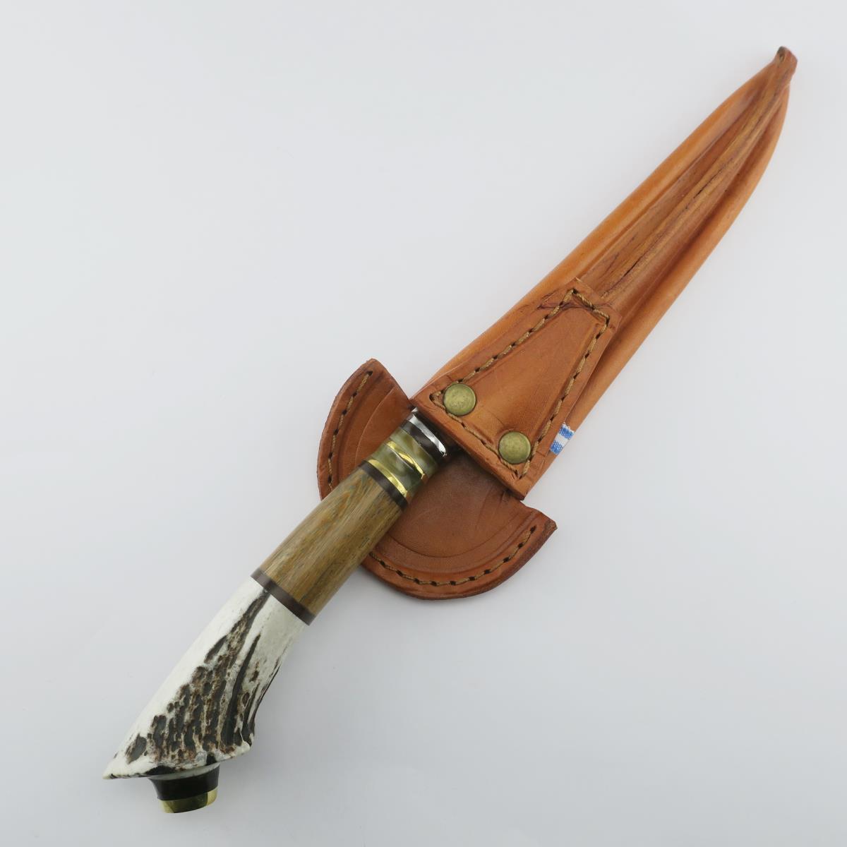 Deer antler handled stainless steel knife with rustic wooden details and brass accents, tucked into a stitched brown leather sheath. Perfect for hunting, camping, or as a collectible, embodying traditional craftsmanship and durability.